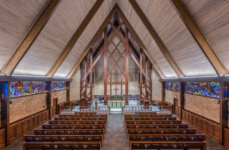 Wide view of the sanctuary at St. Thomas Episcopal Church in Columbus, Georgia, featuring wooden pews, exposed beams, the altar, and colorful stained-glass windows.
